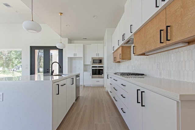 kitchen featuring pendant lighting, backsplash, sink, an island with sink, and white cabinetry