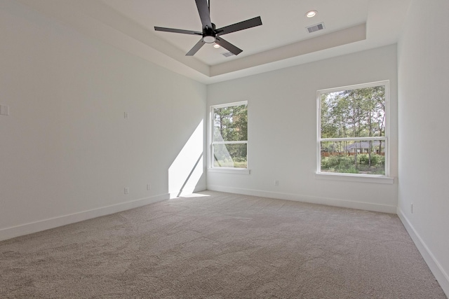 unfurnished room with ceiling fan, light carpet, and a tray ceiling