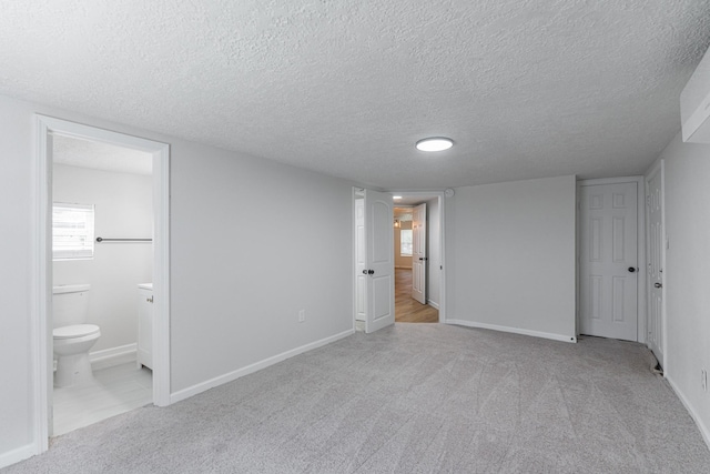 unfurnished bedroom featuring ensuite bathroom, light carpet, and a textured ceiling