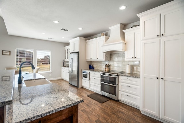 kitchen with custom range hood, stainless steel appliances, white cabinetry, and sink