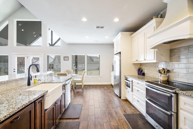 kitchen featuring sink, light stone counters, appliances with stainless steel finishes, white cabinets, and custom exhaust hood