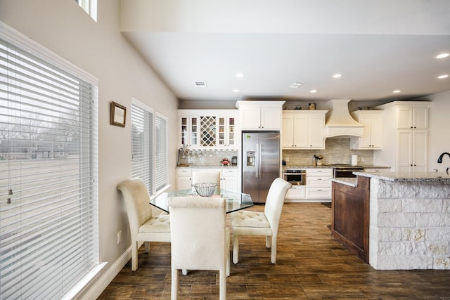 kitchen with white cabinetry, light stone counters, backsplash, custom range hood, and appliances with stainless steel finishes