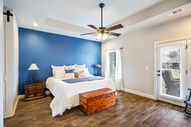 bedroom featuring ceiling fan, a barn door, access to exterior, and a tray ceiling