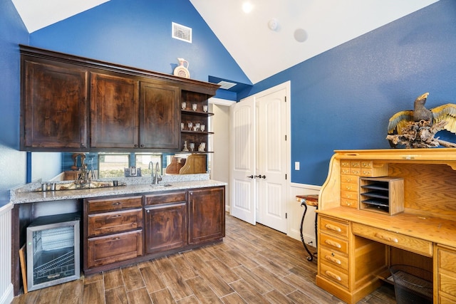 interior space featuring light stone countertops, dark brown cabinets, vaulted ceiling, and sink