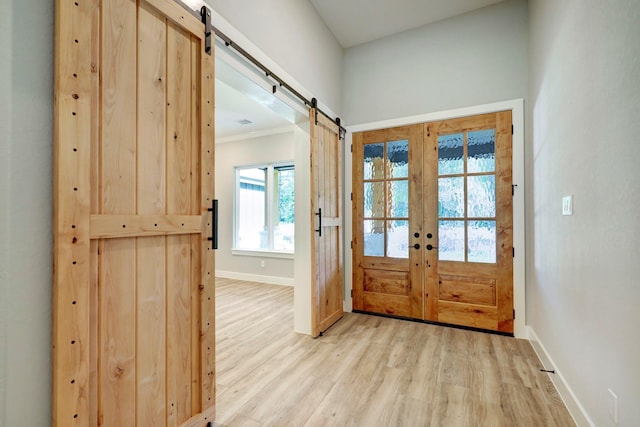 doorway with french doors, light wood-type flooring, a barn door, and ornamental molding