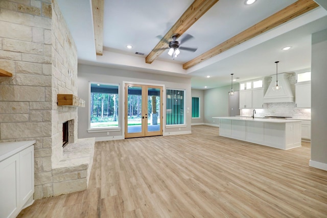 unfurnished living room with french doors, a stone fireplace, ceiling fan, light wood-type flooring, and beam ceiling