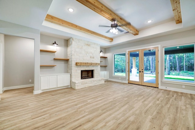 unfurnished living room with french doors, a stone fireplace, ceiling fan, a tray ceiling, and light hardwood / wood-style floors