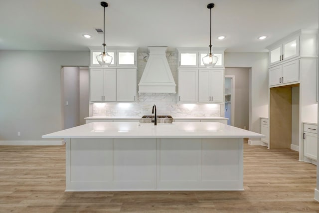 kitchen with white cabinetry, a kitchen island with sink, and custom range hood