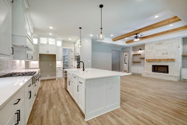 kitchen featuring a fireplace, a center island with sink, white cabinets, and decorative light fixtures