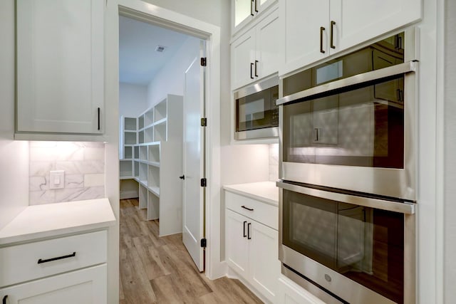 kitchen with white cabinets, decorative backsplash, stainless steel appliances, and light hardwood / wood-style flooring