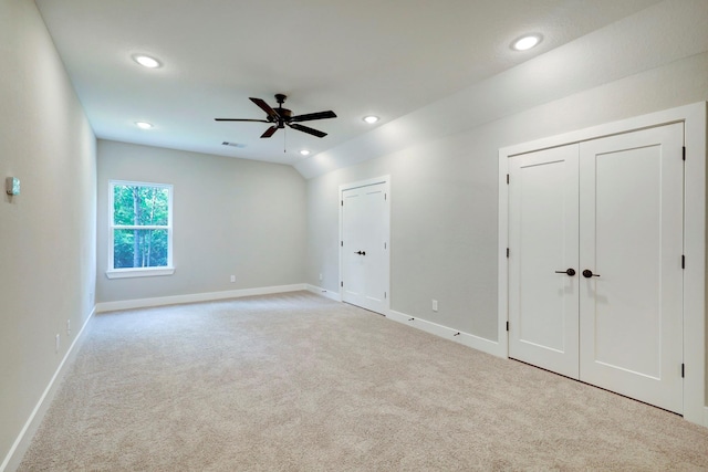 unfurnished bedroom with light carpet, vaulted ceiling, ceiling fan, and multiple closets