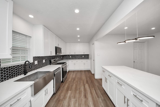 kitchen with sink, white cabinetry, appliances with stainless steel finishes, hardwood / wood-style floors, and decorative backsplash