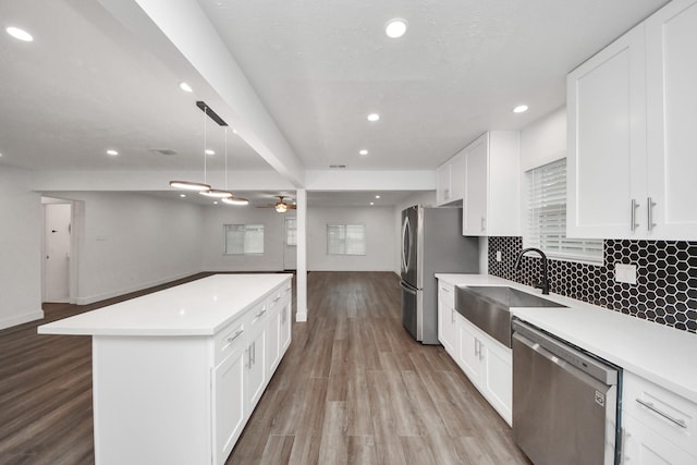 kitchen featuring white cabinetry, hanging light fixtures, stainless steel appliances, light hardwood / wood-style floors, and backsplash