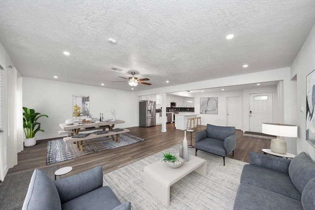 living room featuring ceiling fan, dark wood-type flooring, and a textured ceiling