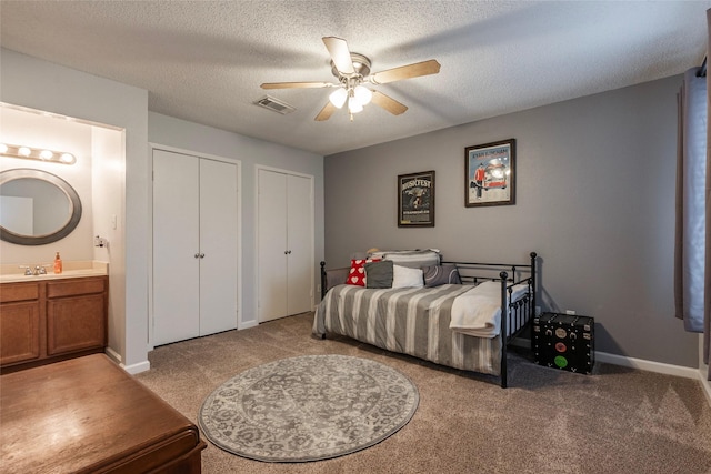 bedroom with a textured ceiling, connected bathroom, two closets, and ceiling fan