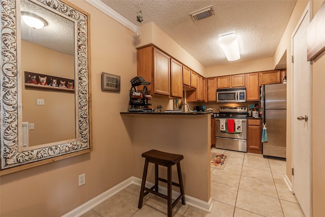 kitchen featuring light tile patterned floors, a textured ceiling, a kitchen bar, kitchen peninsula, and stainless steel appliances