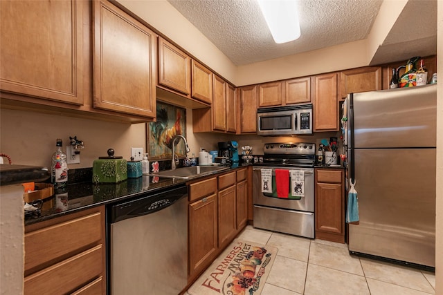 kitchen with sink, stainless steel appliances, dark stone counters, a textured ceiling, and light tile patterned floors