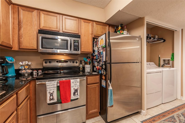 kitchen featuring a textured ceiling, stainless steel appliances, light tile patterned floors, separate washer and dryer, and dark stone countertops