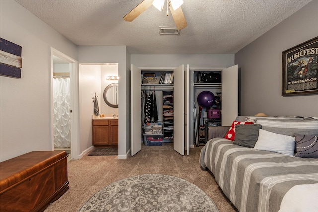 carpeted bedroom with connected bathroom, ceiling fan, two closets, and a textured ceiling