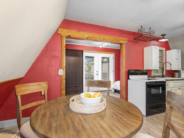 dining space with french doors, sink, light hardwood / wood-style floors, and lofted ceiling