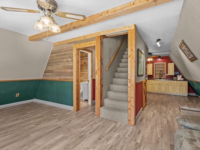 additional living space featuring ceiling fan, sink, lofted ceiling, wooden walls, and light wood-type flooring