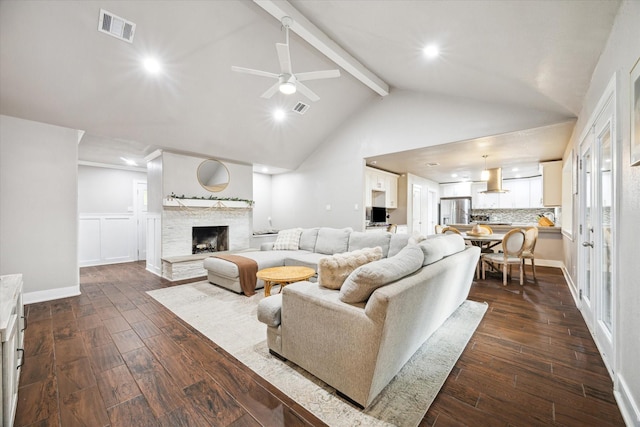 living room with beamed ceiling, dark hardwood / wood-style flooring, a stone fireplace, and ceiling fan