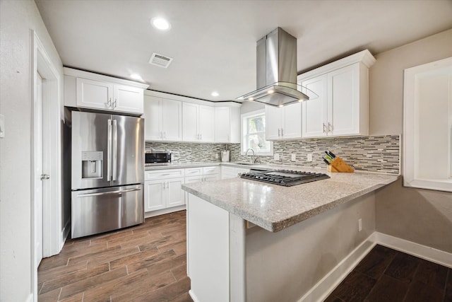 kitchen with backsplash, island range hood, white cabinets, and appliances with stainless steel finishes