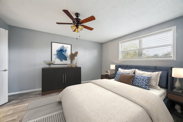 bedroom with ceiling fan, light hardwood / wood-style floors, and a textured ceiling