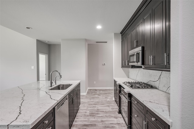 kitchen featuring light stone countertops, sink, light hardwood / wood-style flooring, backsplash, and appliances with stainless steel finishes