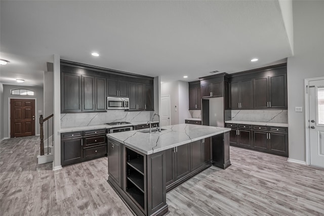 kitchen featuring backsplash, a kitchen island with sink, light stone countertops, and appliances with stainless steel finishes