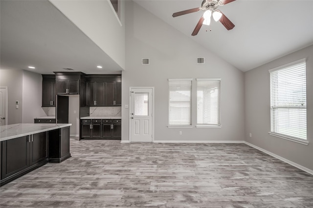 kitchen featuring ceiling fan, light hardwood / wood-style floors, high vaulted ceiling, and tasteful backsplash