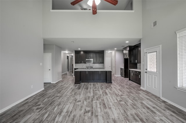 kitchen featuring decorative backsplash, ceiling fan, hardwood / wood-style flooring, a center island with sink, and a high ceiling