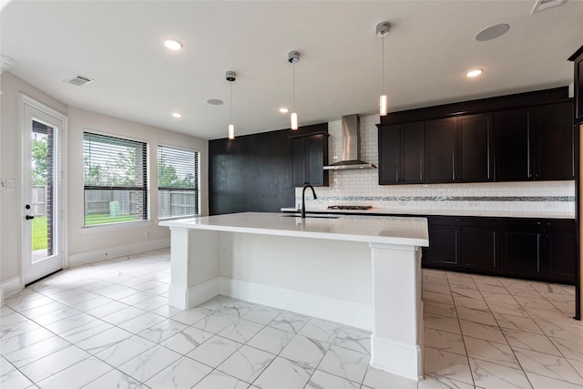 kitchen featuring an island with sink, sink, wall chimney exhaust hood, and pendant lighting