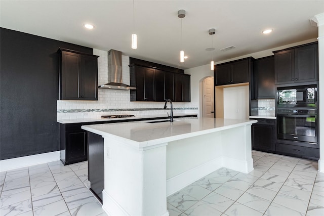 kitchen featuring black appliances, wall chimney range hood, sink, and an island with sink