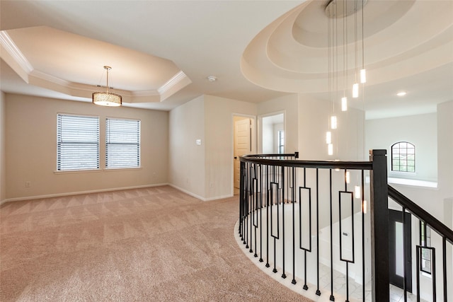 corridor with light colored carpet, crown molding, and a tray ceiling