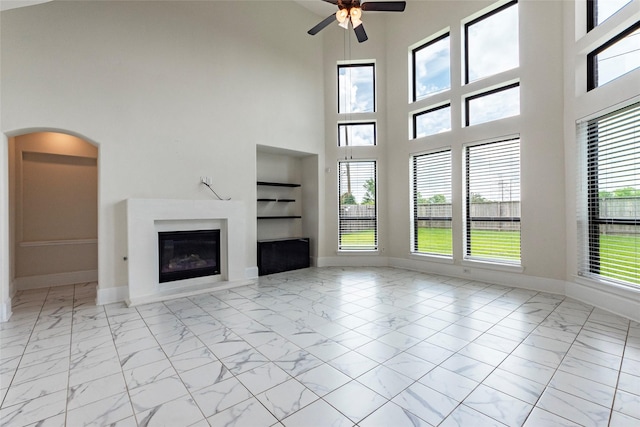 unfurnished living room with built in shelves, ceiling fan, and a high ceiling