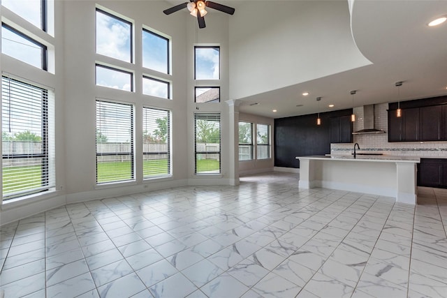 unfurnished living room with ceiling fan, a towering ceiling, sink, and decorative columns