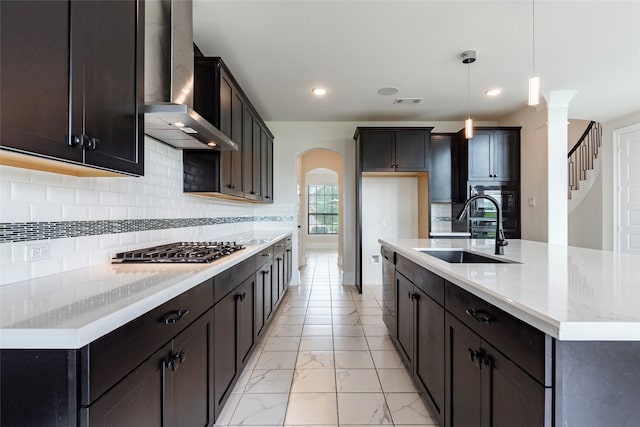 kitchen featuring wall chimney exhaust hood, stainless steel appliances, sink, decorative light fixtures, and a center island with sink