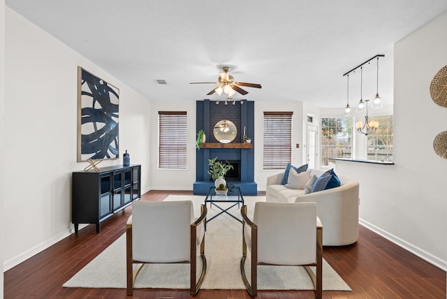 living room featuring ceiling fan with notable chandelier, a large fireplace, and dark wood-type flooring