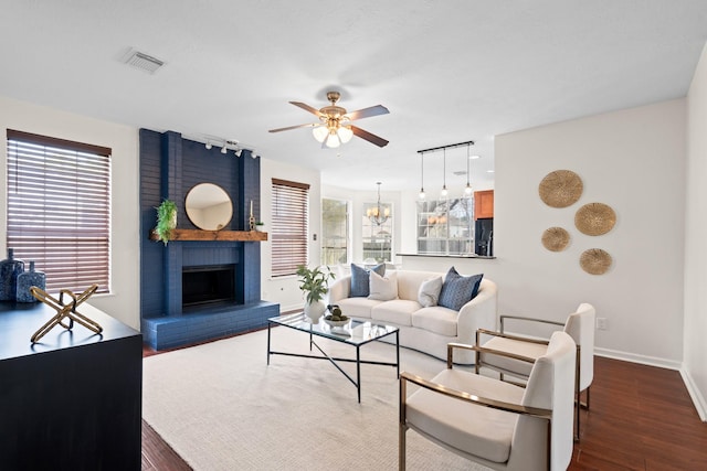 living room with hardwood / wood-style floors, ceiling fan with notable chandelier, and a brick fireplace