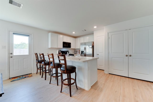 kitchen with a breakfast bar, black appliances, white cabinets, light wood-type flooring, and kitchen peninsula