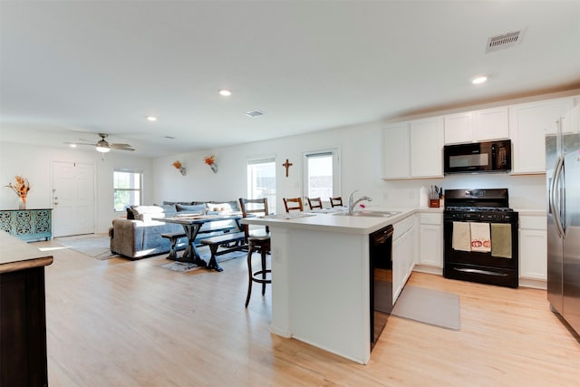 kitchen featuring white cabinetry, ceiling fan, light hardwood / wood-style flooring, a breakfast bar, and black appliances