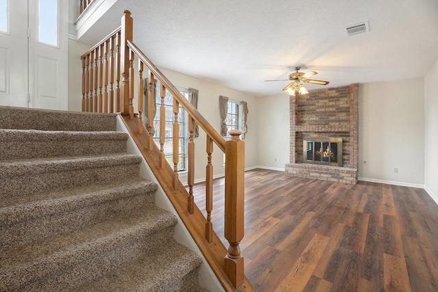 staircase featuring a fireplace, hardwood / wood-style floors, a textured ceiling, and ceiling fan