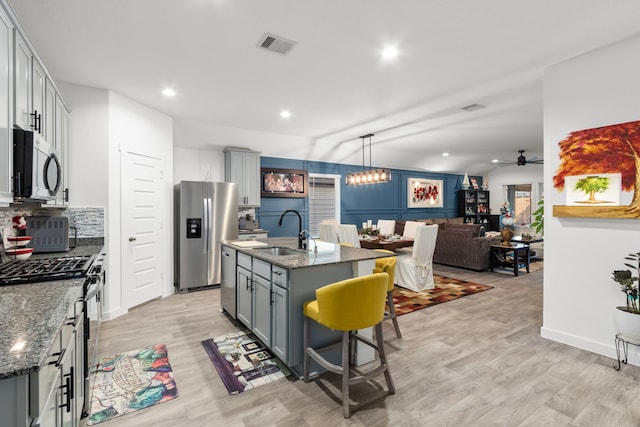 kitchen with sink, vaulted ceiling, a kitchen bar, a center island with sink, and appliances with stainless steel finishes