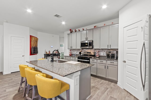 kitchen with gray cabinetry, a breakfast bar, sink, an island with sink, and stainless steel appliances