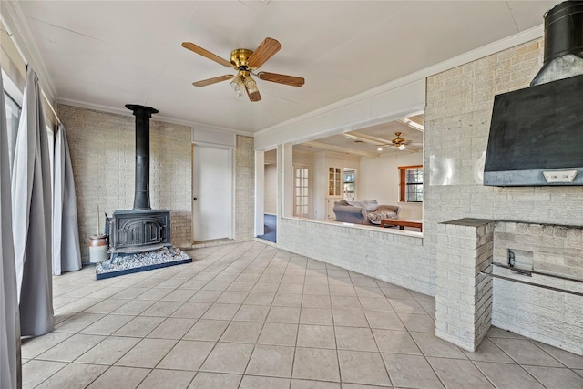 unfurnished living room with ceiling fan, ornamental molding, light tile patterned floors, and a wood stove