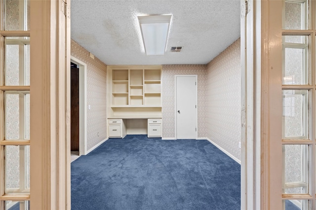 unfurnished office with built in desk, dark carpet, and a textured ceiling