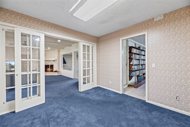 carpeted spare room featuring a textured ceiling, a fireplace, and french doors