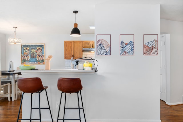 kitchen featuring dark hardwood / wood-style flooring, kitchen peninsula, backsplash, and hanging light fixtures