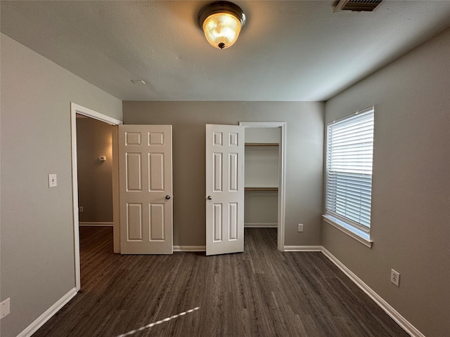 unfurnished bedroom with a closet, dark wood-type flooring, and a spacious closet